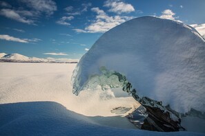 A large ice formation in a snowy landscape with distant mountains.