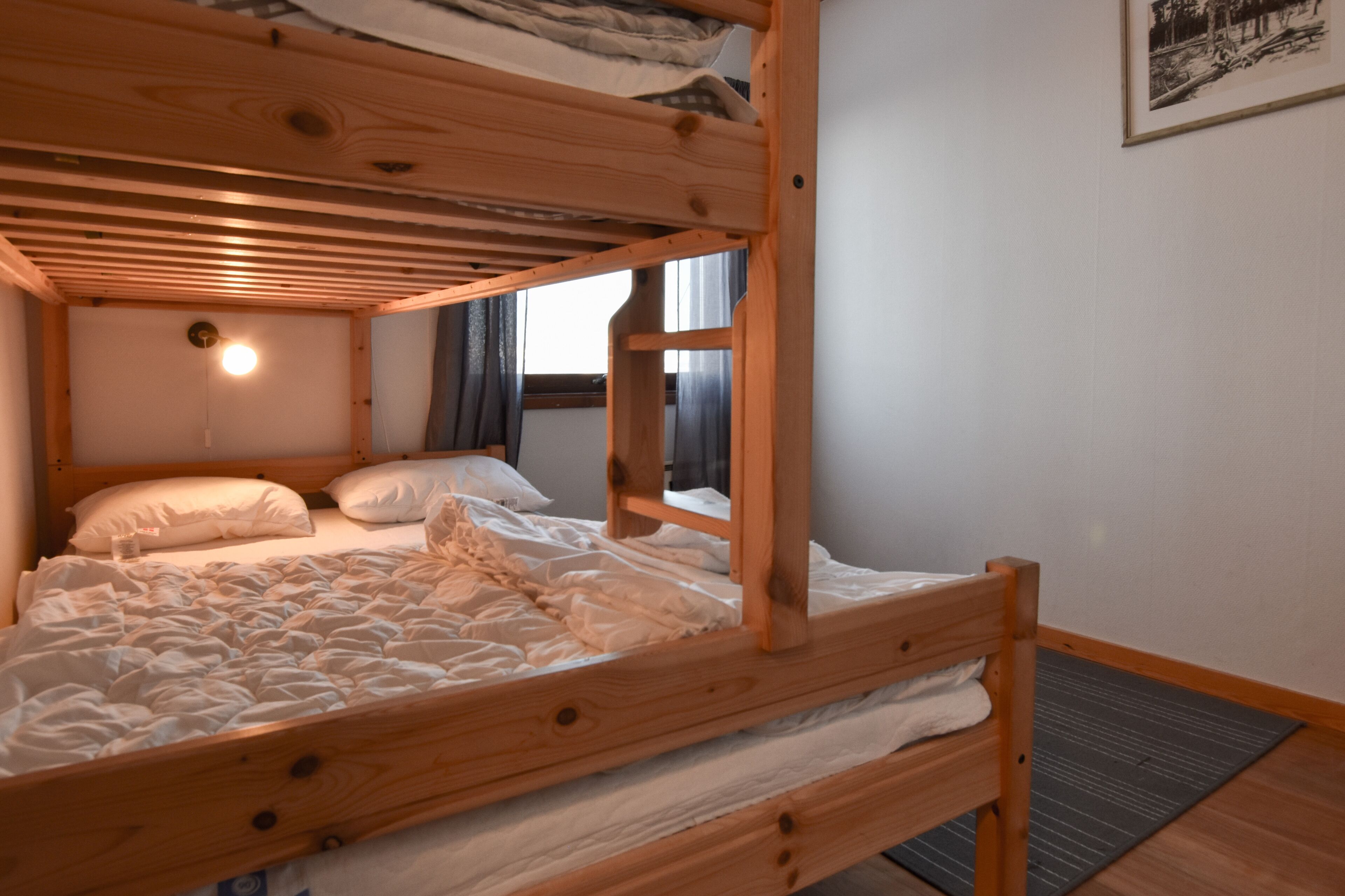 Un letto a castello con struttura in legno, biancheria da letto bianca e un punto luce sopra la testiera.