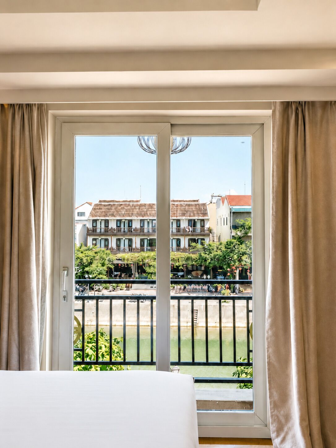 A hotel room with a balcony, a bed, and a view of buildings and greenery.