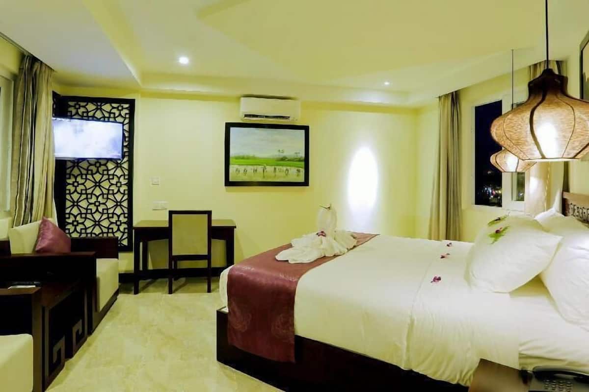Una habitación de hotel con una cama, un escritorio, una silla, un televisor y un cuadro en la pared.