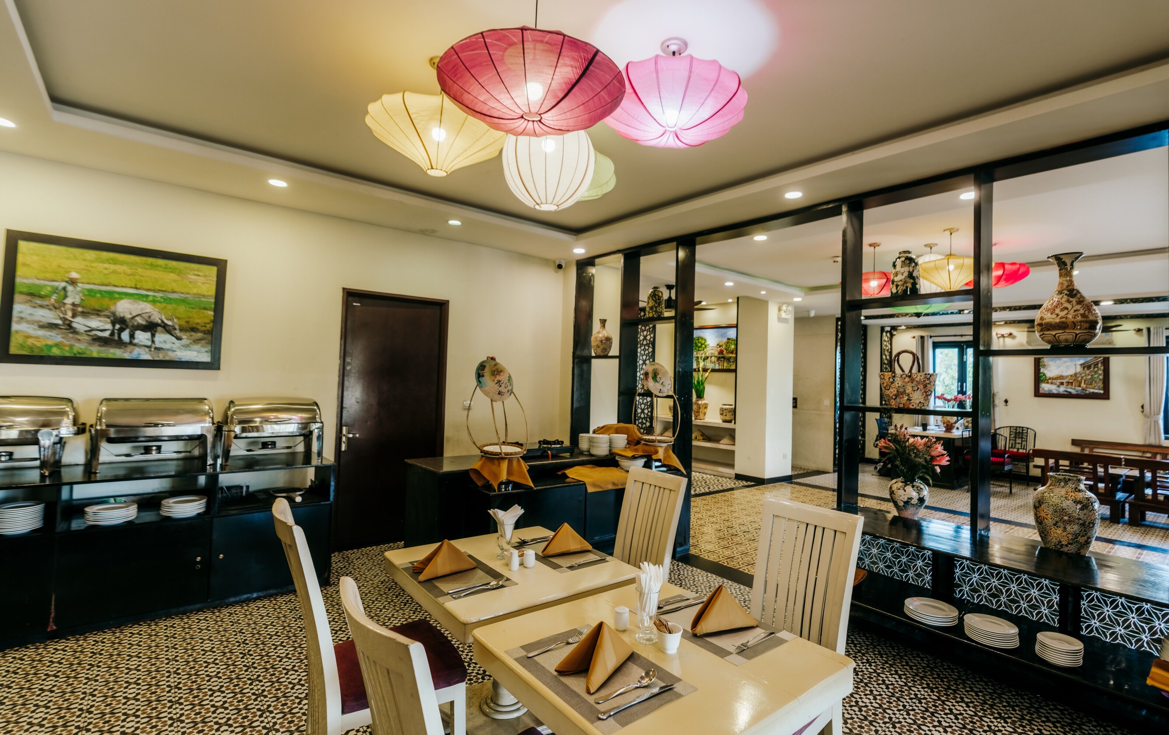 A dining area with tables set for service, a buffet line, and a view through a glass partition to another room.