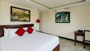 Ein Hotelzimmer mit einem großen Bett, zwei Bildern an den Wänden, einer roten Pendelleuchte und einem kleinen Tisch mit einer Fernbedienung.