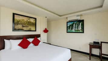 A hotel room with a large bed, two paintings on the walls, a red pendant light, and a small table with a remote control.