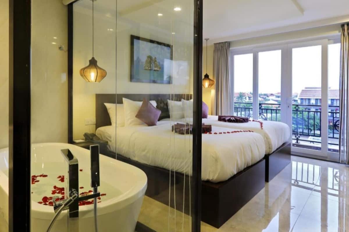 Una habitación de hotel moderna con una cama grande, una bañera con pétalos de rosa, un balcón con vistas y un cuadro en la pared.
