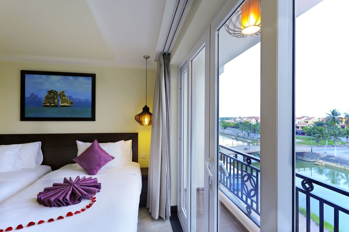 Une chambre d’hôtel avec un lit, un tableau, un balcon donnant sur un plan d’eau et des bâtiments.