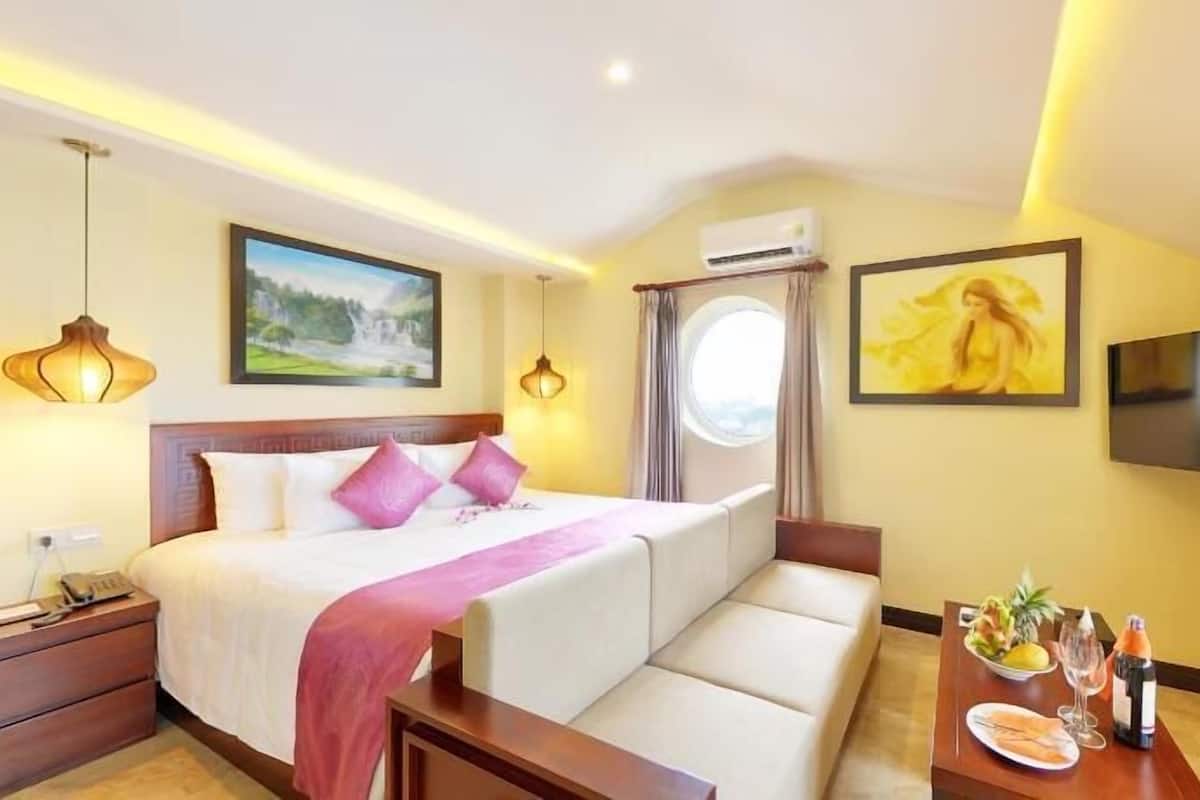 Una habitación de hotel con cama, televisor, una mesa de comedor y frutero, y ventana con cortinas.