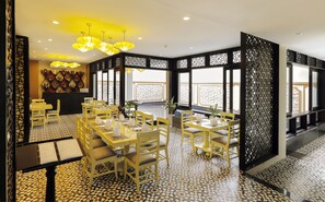 A dining area with yellow chairs and tables, a patterned floor, and a view of the sea through large windows.