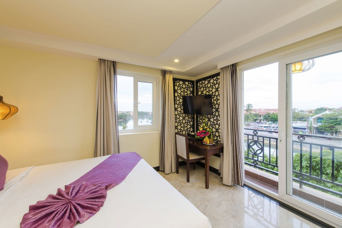 Une chambre d’hôtel avec un grand lit, un bureau avec une télévision et un balcon offrant une vue sur la ville.
