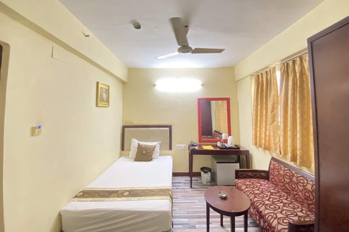 Ein Hotelzimmer mit Bett, kleinem Tisch, Sofa, Spiegel und Deckenventilator.