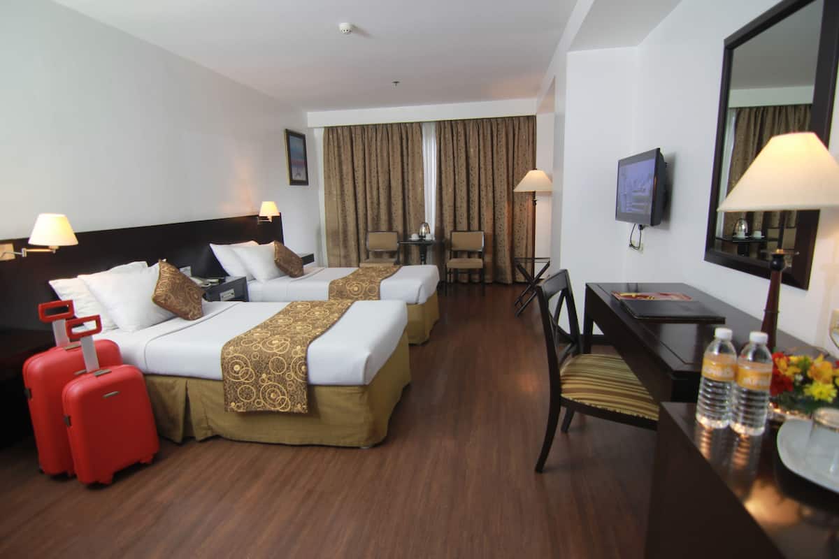 Een hotelkamer met twee bedden, een bureau, een stoel, een televisie en een raam met gordijnen.