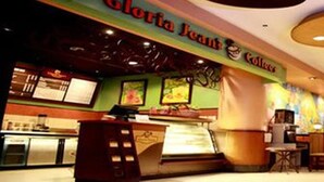 Un restaurante con mostrador y zona de mesas, decorado con murales coloridos y un letrero que dice "Gloria Jean's".