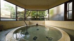 Ein Whirlpool in einem Zimmer mit großen Fenstern, Holzboden und Blick auf Grünfläche.