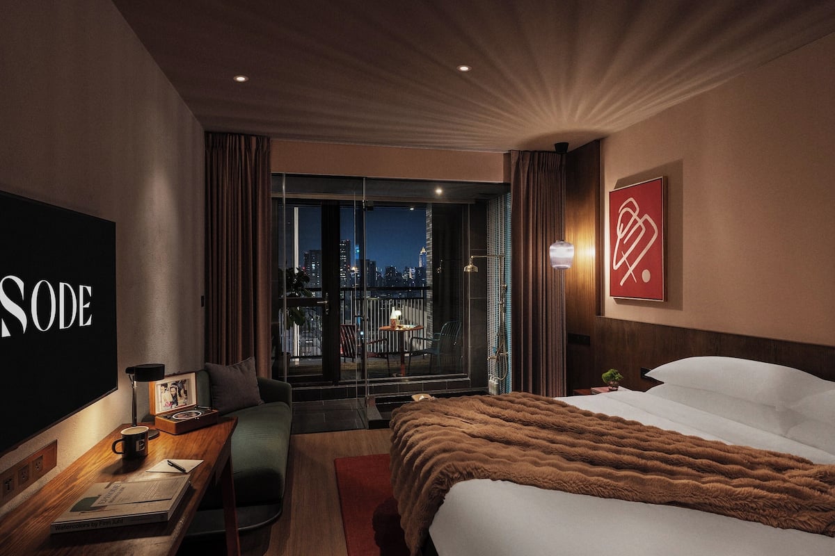 A hotel room with a large bed, a desk with a lamp, a chair, and a view of the city at night.