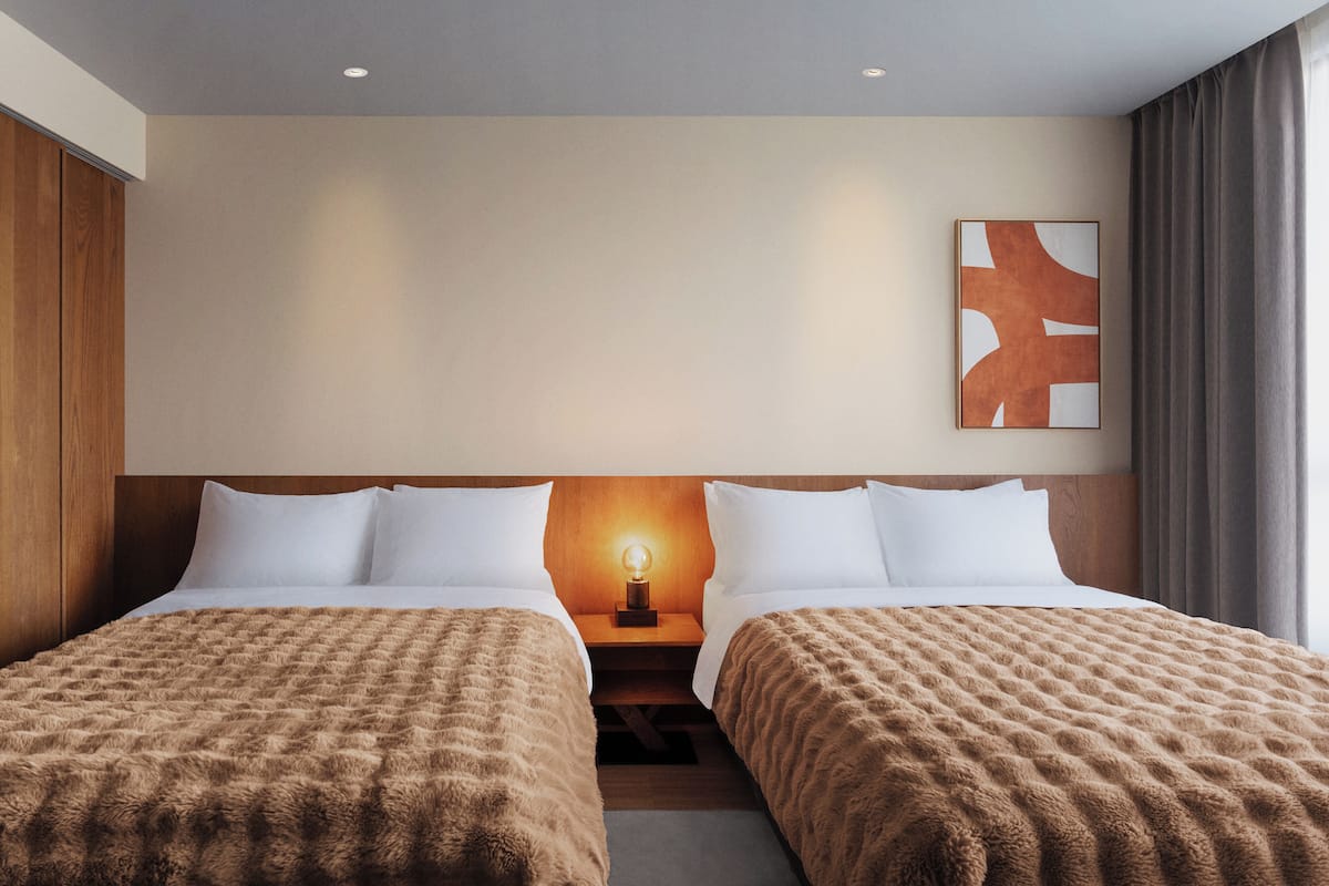 A hotel room with two beds, a nightstand with a lamp, a wooden headboard, and a painting on the wall.