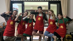 A group of people in red aprons posing in a room with a sliding glass door leading to a balcony. - Jolie Villa Hoi An (Da Nang)
