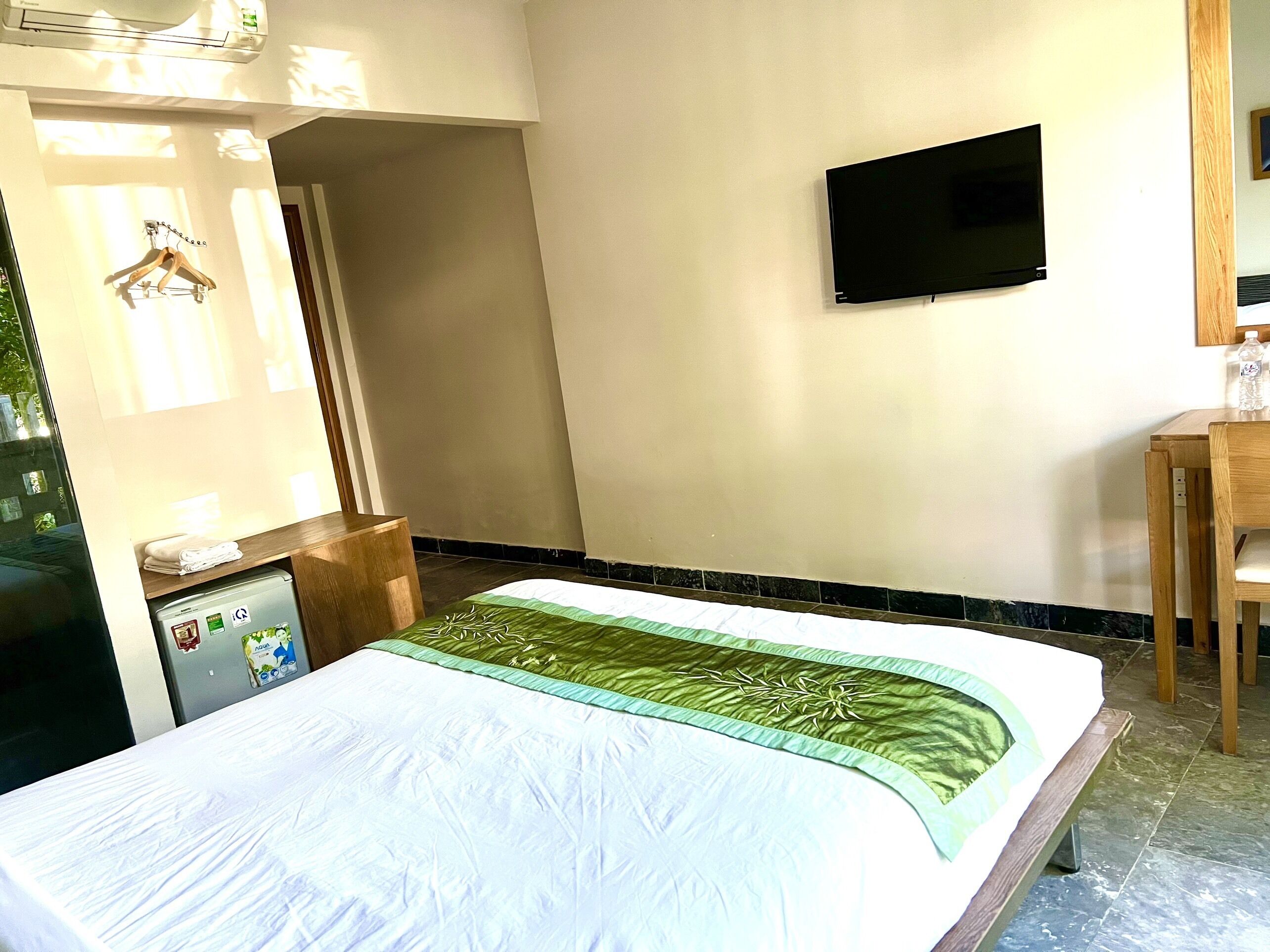 A hotel room with a bed, a TV mounted on the wall, a small desk, and a wardrobe.