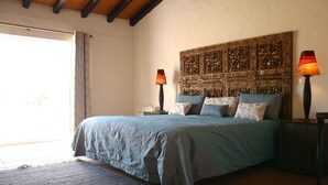 A bedroom with a large bed, two bedside lamps, a decorative headboard, and a view of the outdoors. - Monte das Faias (Grandola)