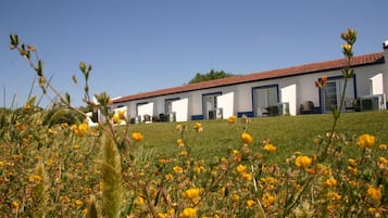 A building with a red-tiled roof and white walls, surrounded by a grassy field with yellow flowers.