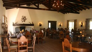 A spacious dining area with wooden tables and chairs, a fireplace, and decorative wall sconces. - Monte das Faias (Grandola)