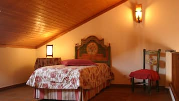 A bedroom with a wooden ceiling, a bed with floral bedding, a chair with a red cover, and a wall-mounted light fixture.