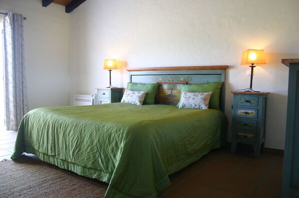 A bed with a green bedspread, two bedside tables with lamps, and a small dresser with floral patterns.