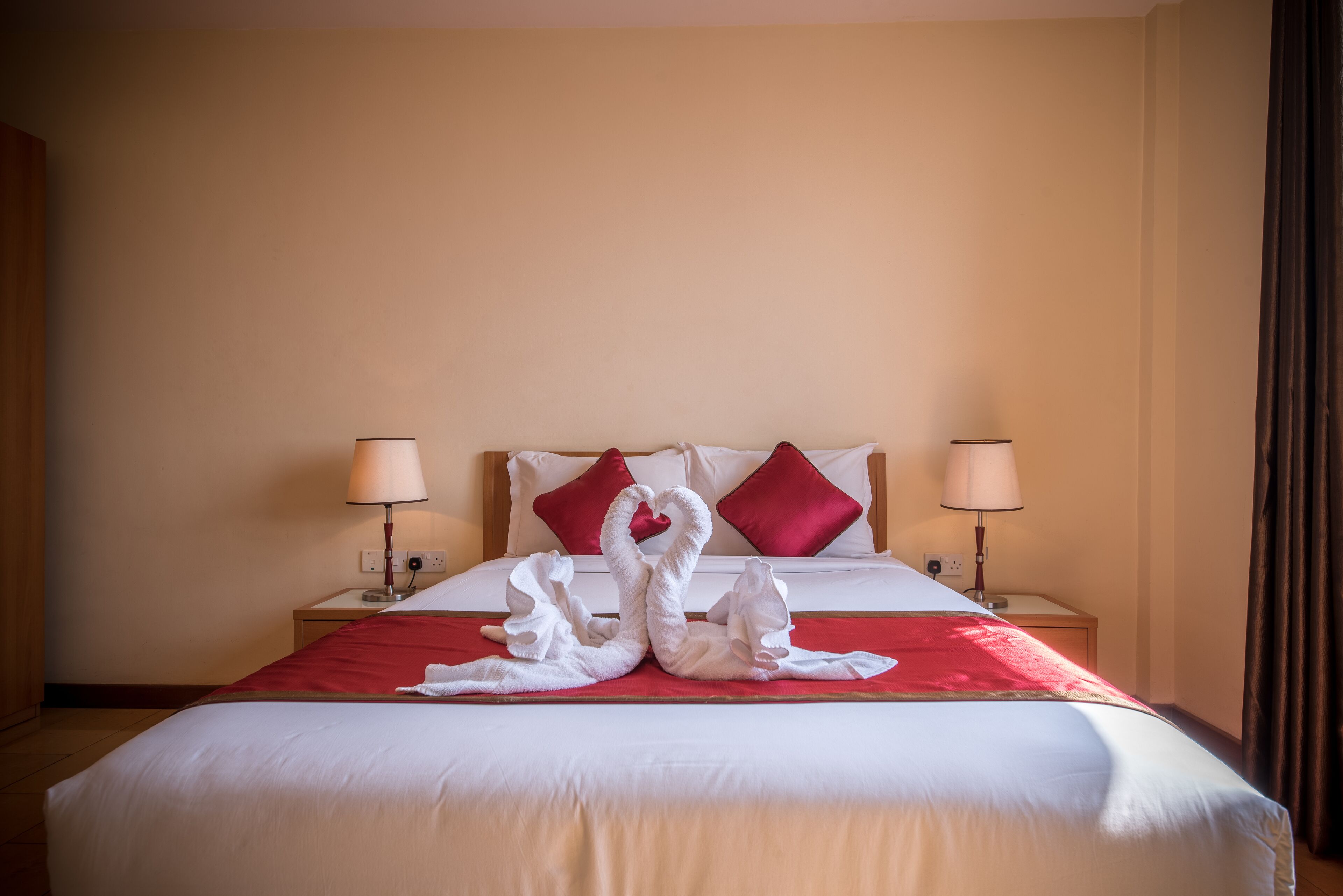 Ein Hotelzimmer mit einem ordentlich bezogenen Bett, roten und weißen Kissen und zwei Nachttischlampen.