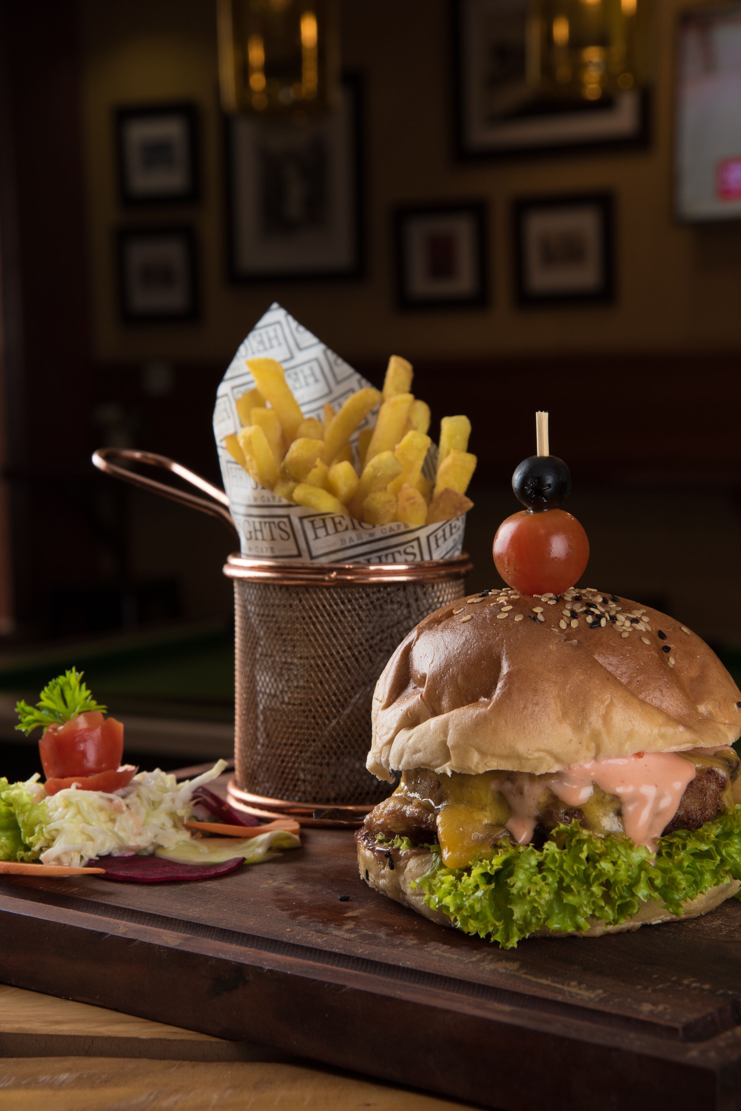 Een hamburger met frietjes en een kleine tomaat op een broodje, vergezeld van een salade en augurken.