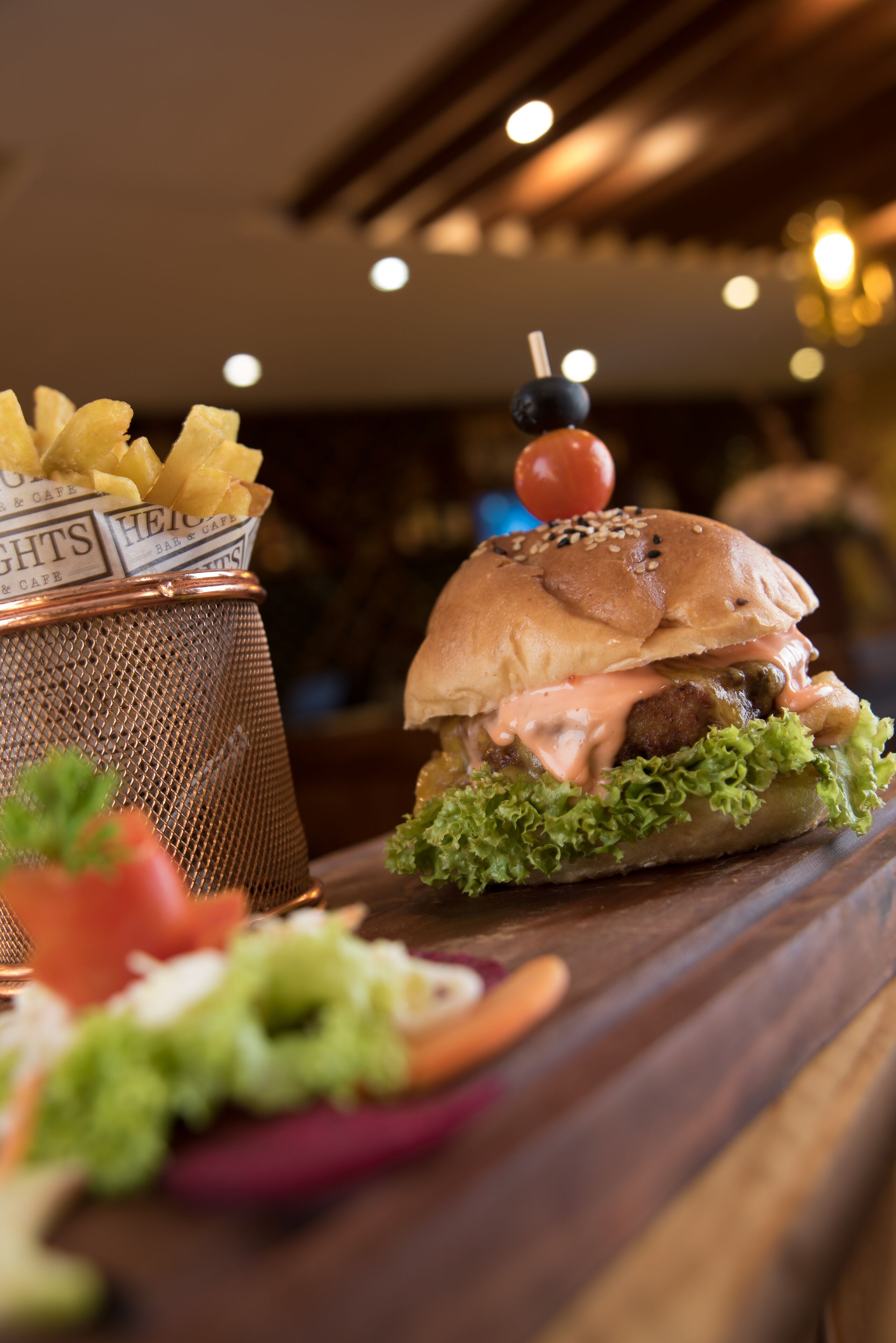 A burger with lettuce, a bun, and a sauce, alongside a basket of fries.