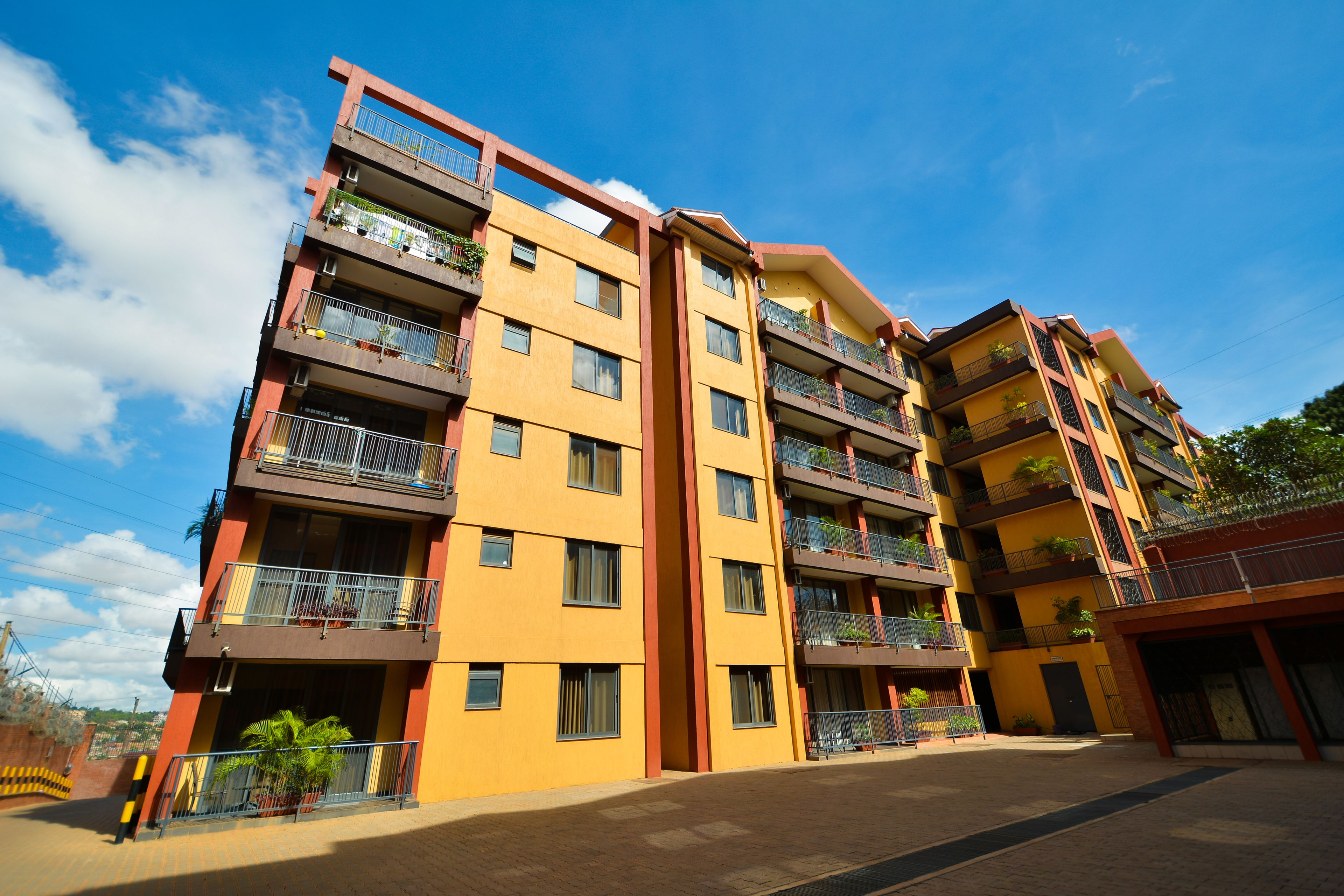 A multi-story residential building with balconies, a central entrance, and a paved courtyard.