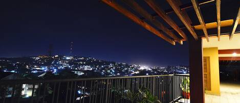 A balcony with a metal railing overlooking a cityscape at night.
