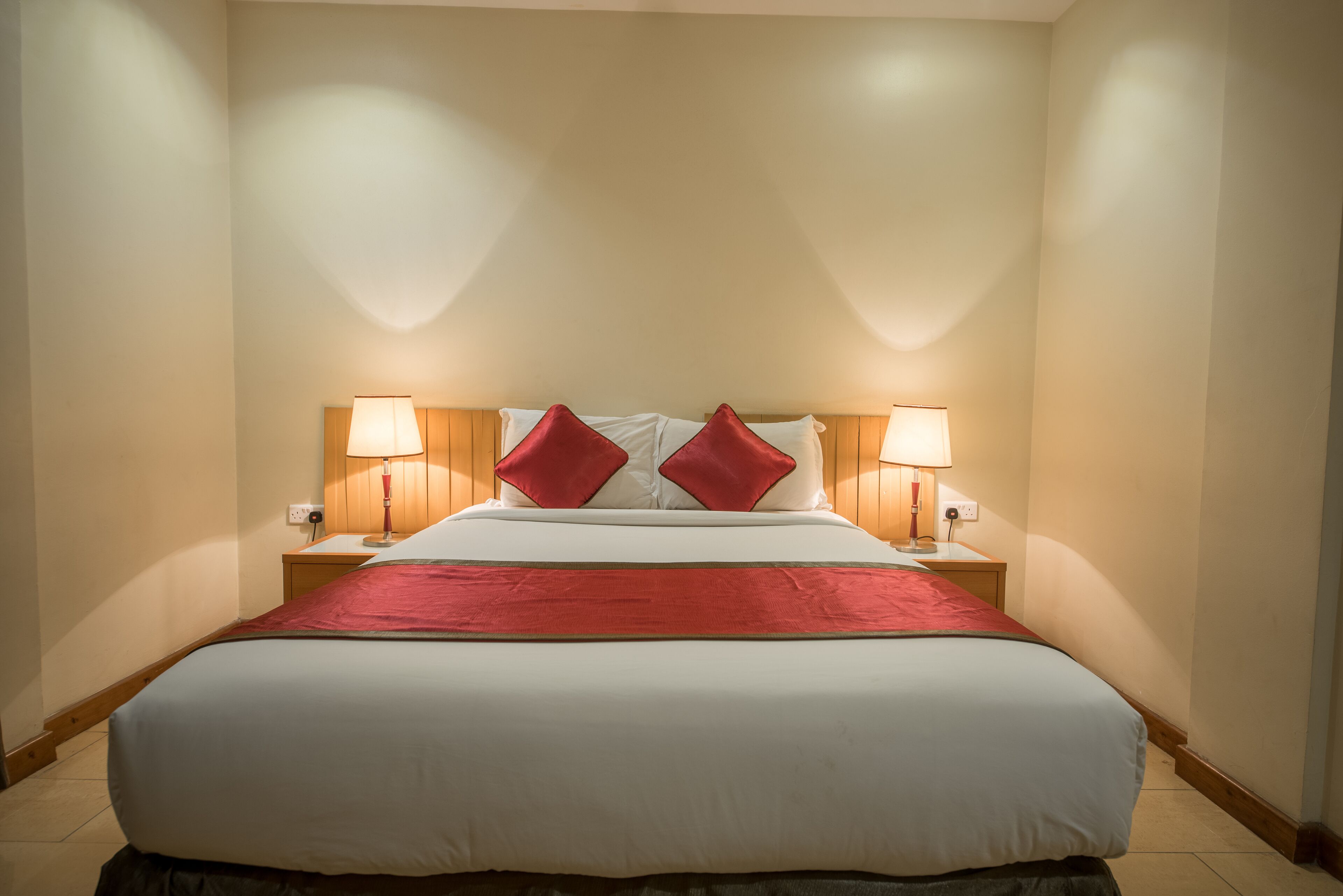 A neatly made bed with a red bedspread and two red pillows, flanked by two bedside lamps on wooden nightstands.