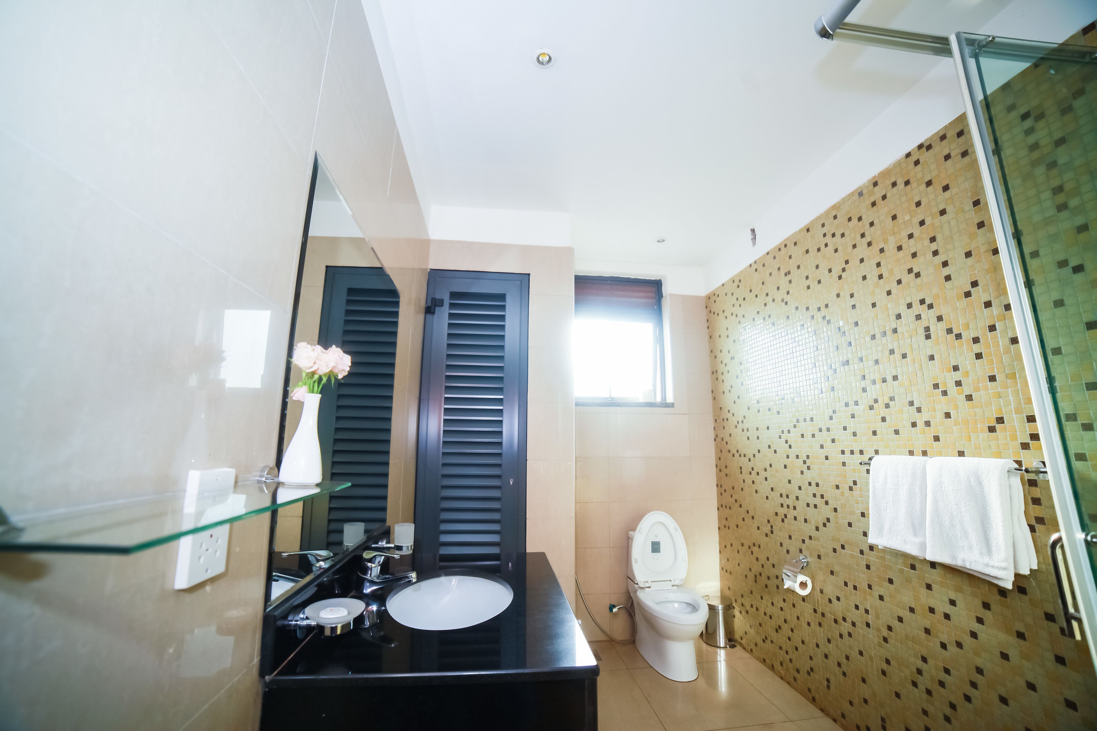 A modern bathroom with a glass shelf, a black sink, a toilet, and a shower area.