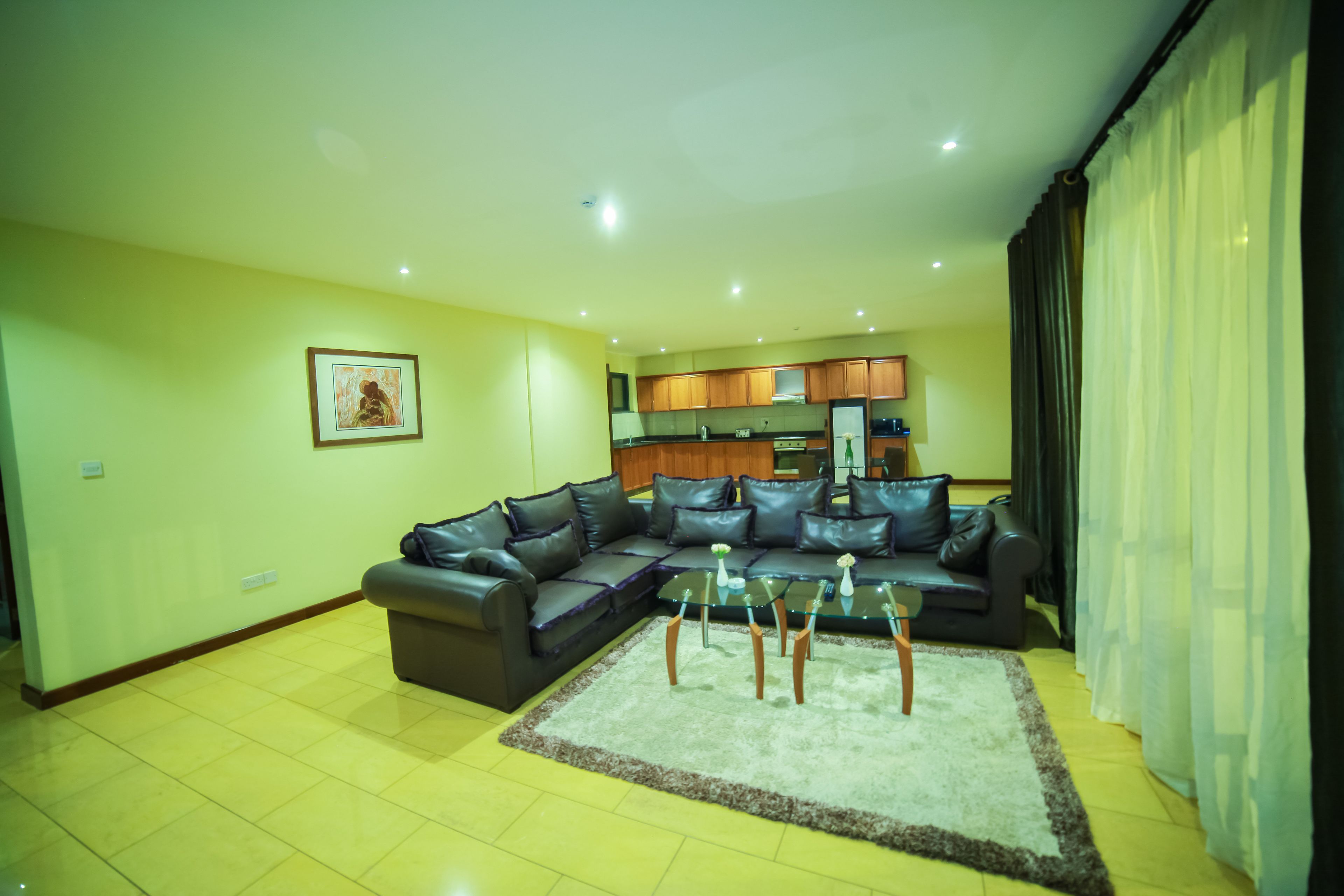 A living room with a sectional sofa, a glass coffee table, and a kitchen in the background.