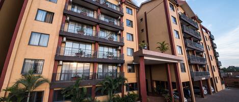 A multi-story hotel with balconies, a parking area, and a landscaped entrance.