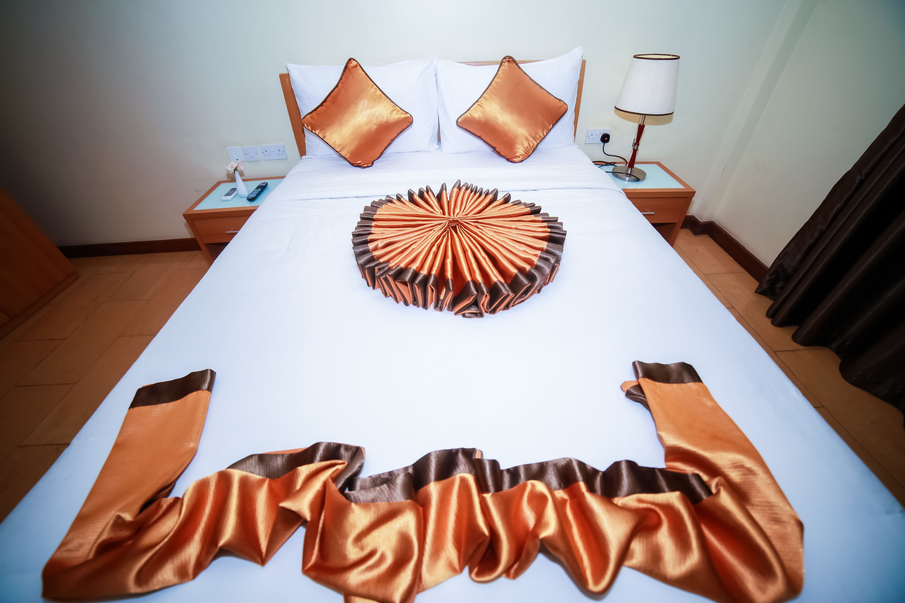 A neatly made bed with a decorative pillow arrangement, a bedside table with a lamp, and a power outlet.