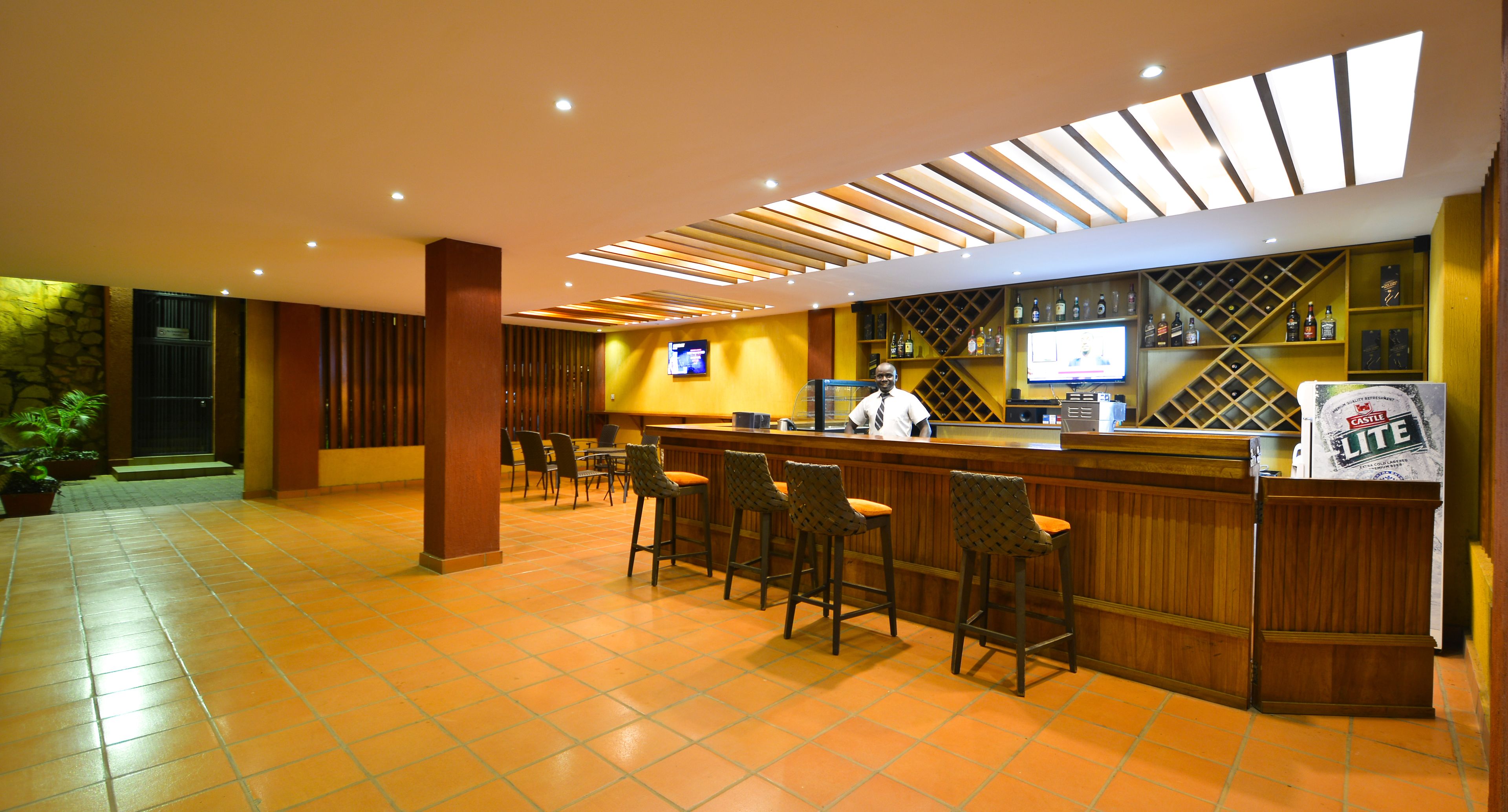 A bar area with wooden bar stools, a television screen, and a Castle Lite beer dispenser.