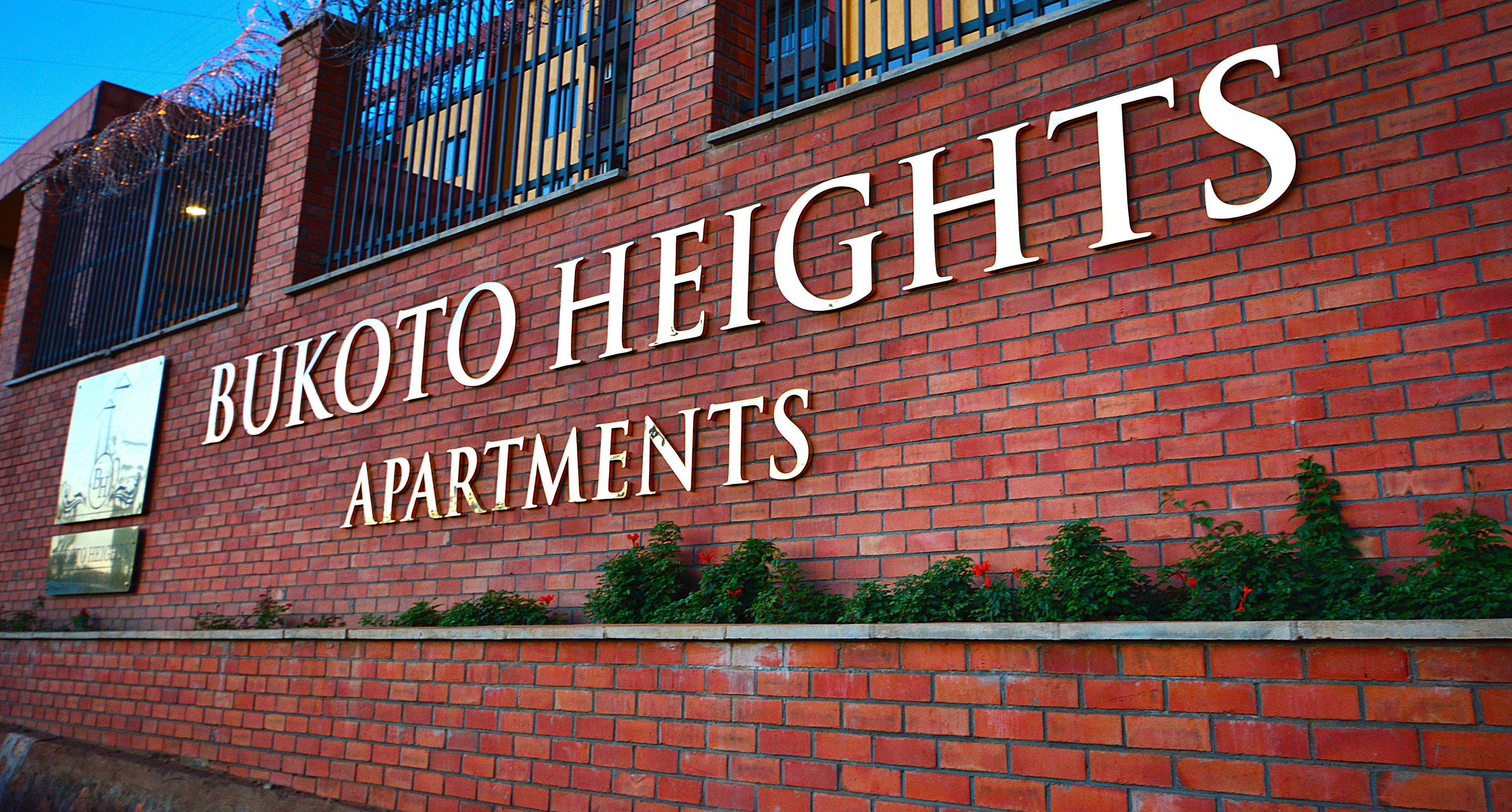 A brick building with the sign "BUKOTO HEIGHTS APARTMENTS" indicating a residential complex.