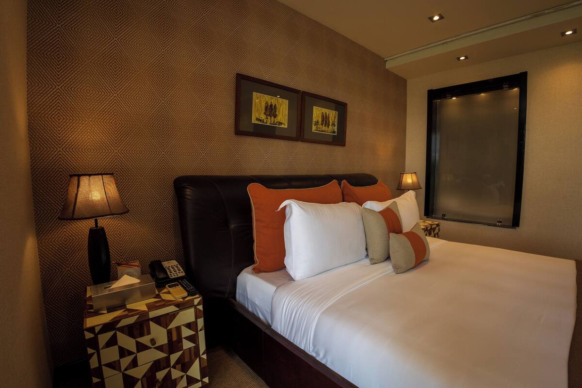 Habitación de hotel con una cama grande, dos cuadros en la pared, una mesita de noche con lámpara y un papel tapiz estampado.
