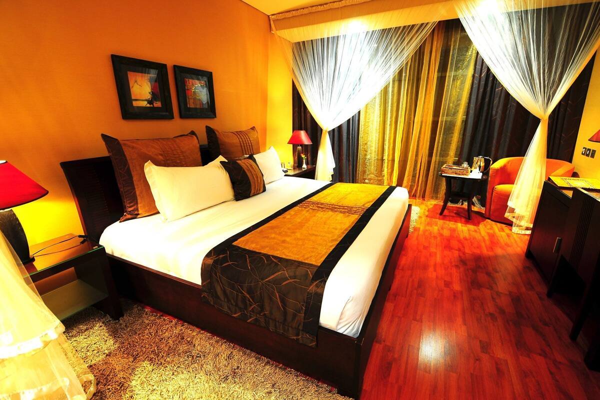 Habitación de hotel con una cama grande, una mesita de noche, una silla, una pequeña mesa y una cortina.