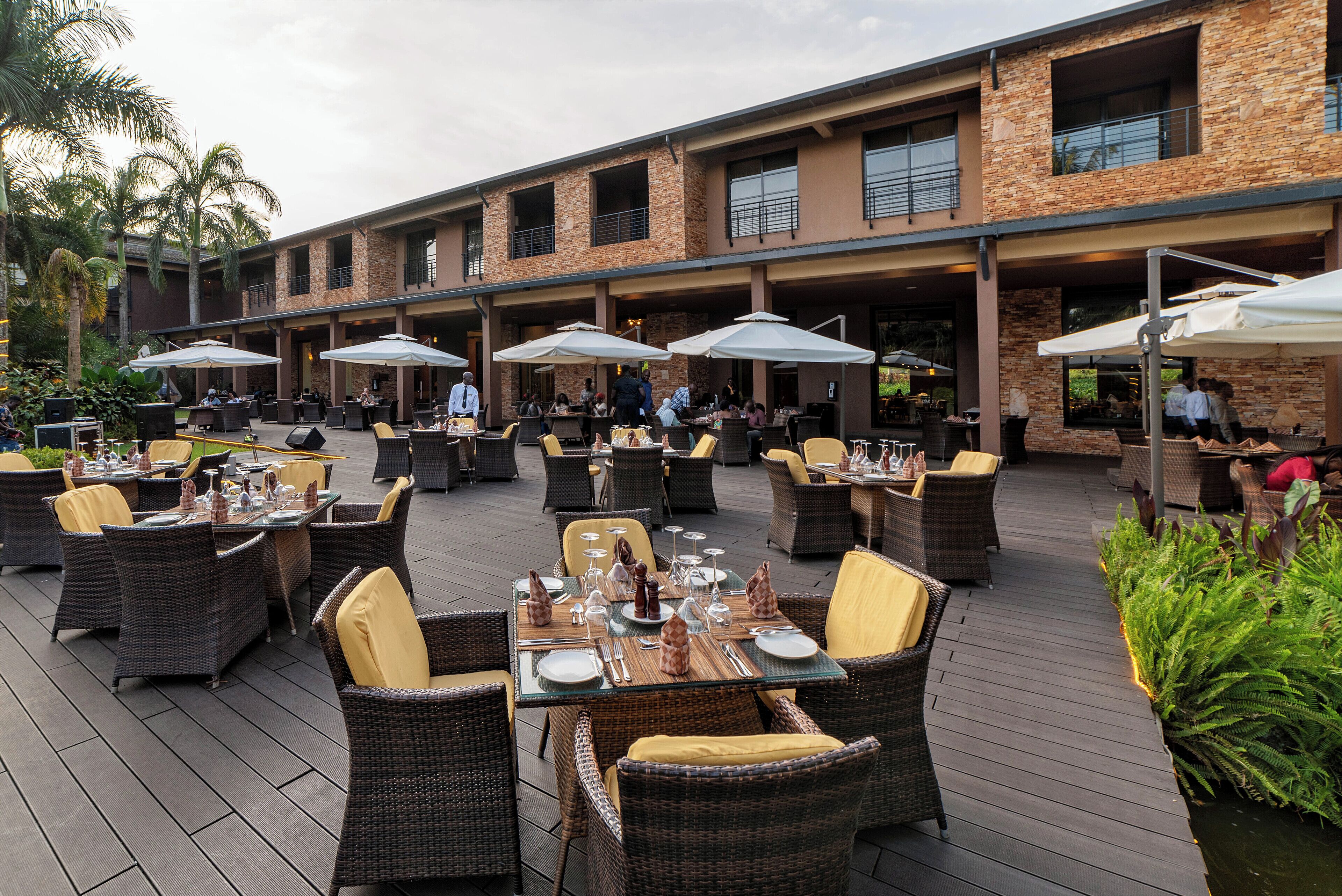 An outdoor dining area with wicker furniture and umbrellas, set against a building with stone and brickwork.