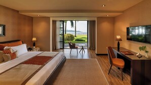 Habitación de hotel con una cama grande, un escritorio, una silla, un televisor y vistas a un jardín y al agua.