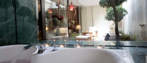 Ein modernes Badezimmer mit einer großen Badewanne, einer in Glaswände gefassten Dusche und einer Sitzecke mit Baum und Lampen.