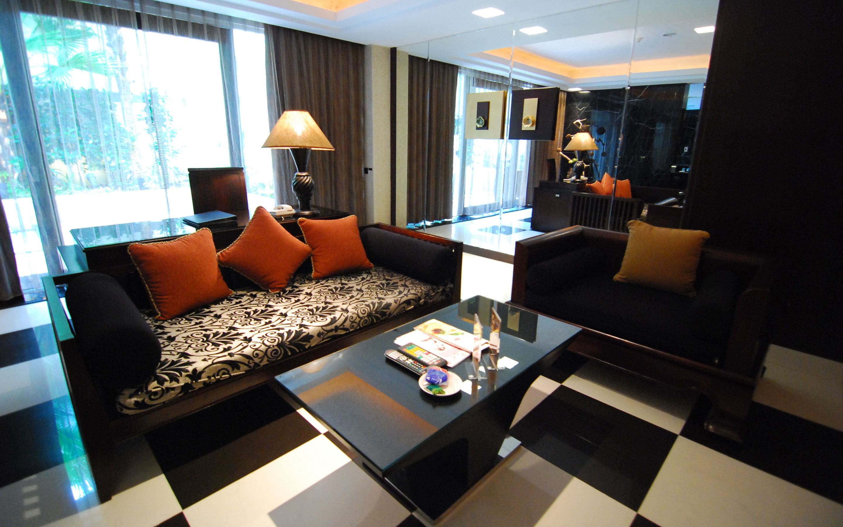 Ein modernes Wohnzimmer mit einem schwarz-weißen Schachbrettfußboden, einem gemusterten Sofa mit orangenen Kissen und einem Couchtisch mit Fernbedienungen und einem Glas.