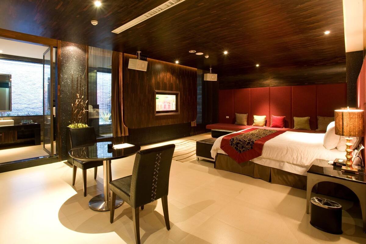 A modern hotel room with a large bed, a desk, and a view of the sea.