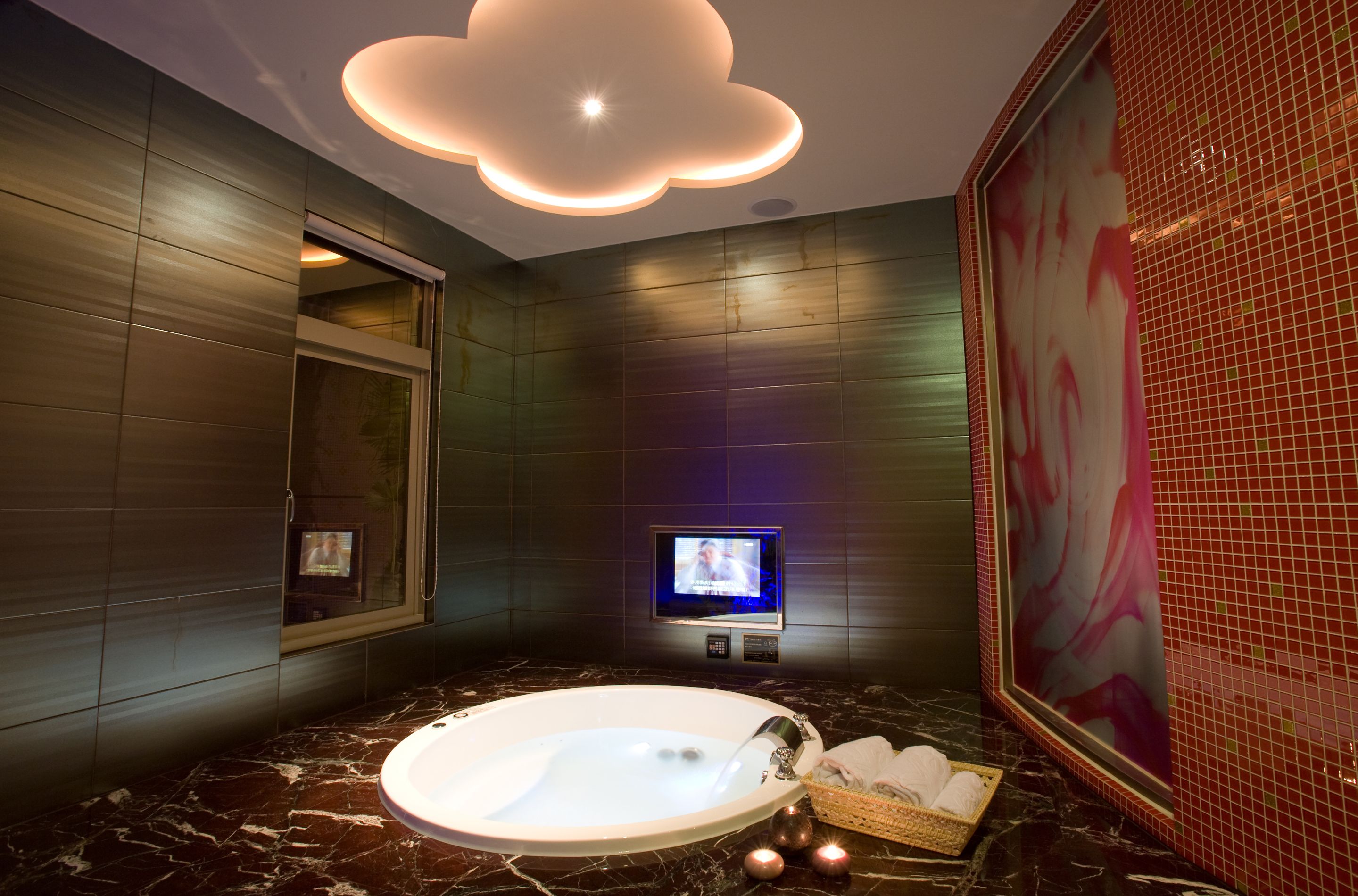 A modern bathroom with a marble floor, a large bathtub, a wall-mounted TV, and a ceiling light fixture.