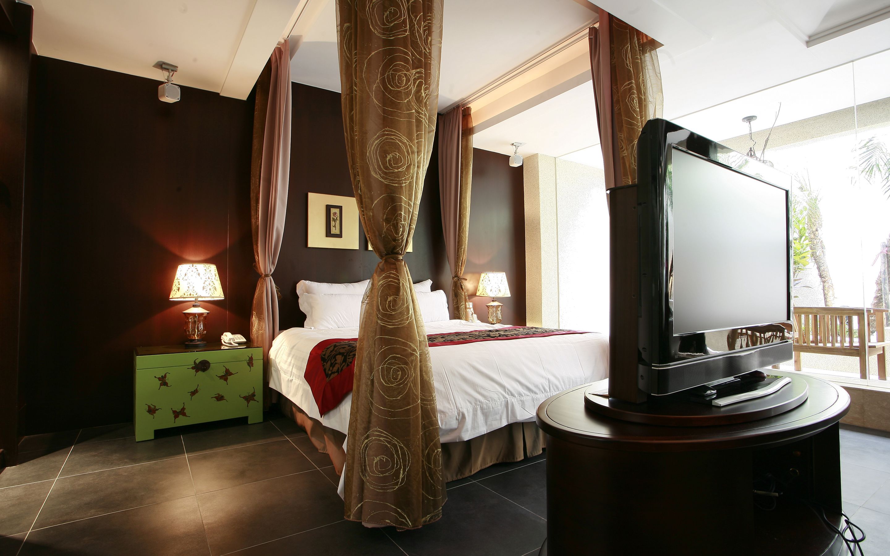 A bedroom with a bed, curtains, a television, and a nightstand with a lamp.