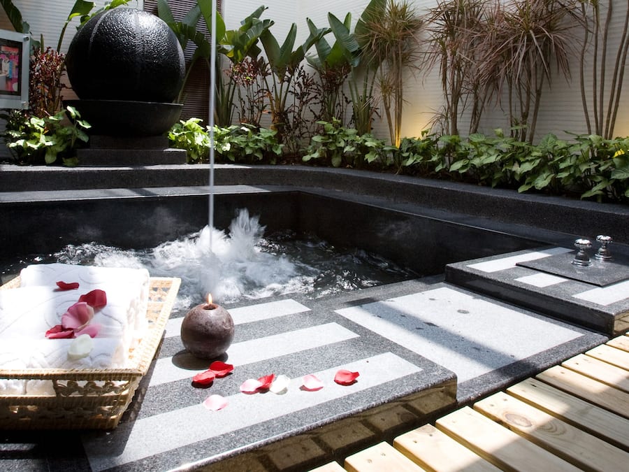 Ein Whirlpool mit Steintonne, umgeben von Pflanzen und einer Holzterrasse.