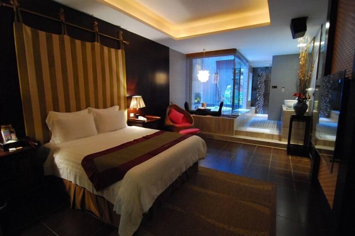 A hotel room with a large bed, a desk with a lamp, a chair, a bathroom with a bathtub, and a view of the outdoors.