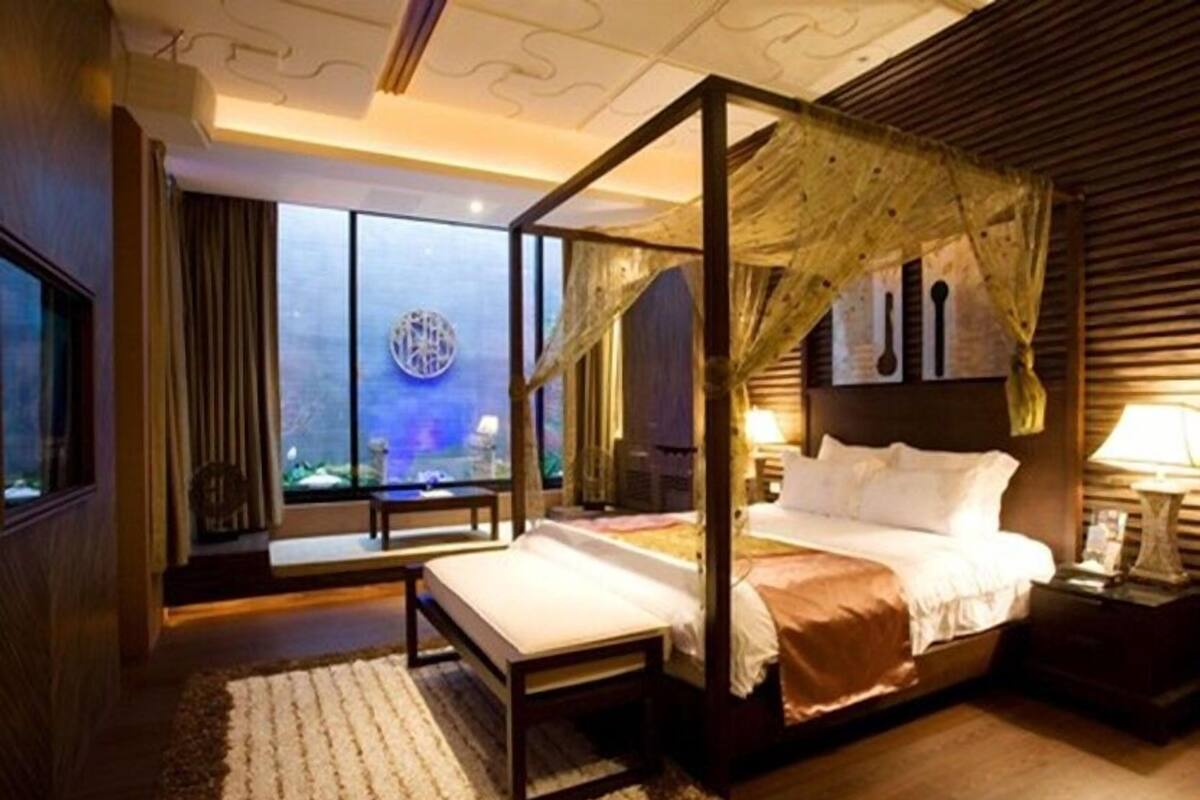 A four-poster bed with a canopy, a large window with a view, and a bedside table with a lamp.