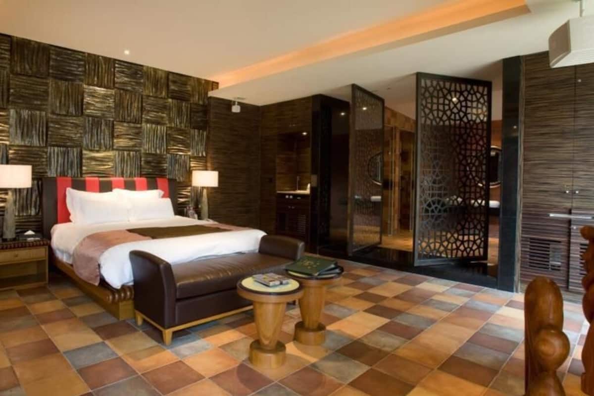 A hotel room with a large bed, a nightstand, a bedside table, a wooden chair, and a decorative screen.